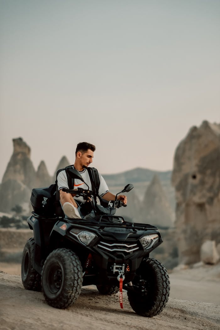 Young man riding an ATV through rocky landscape at sunset, showcasing adventure travel.